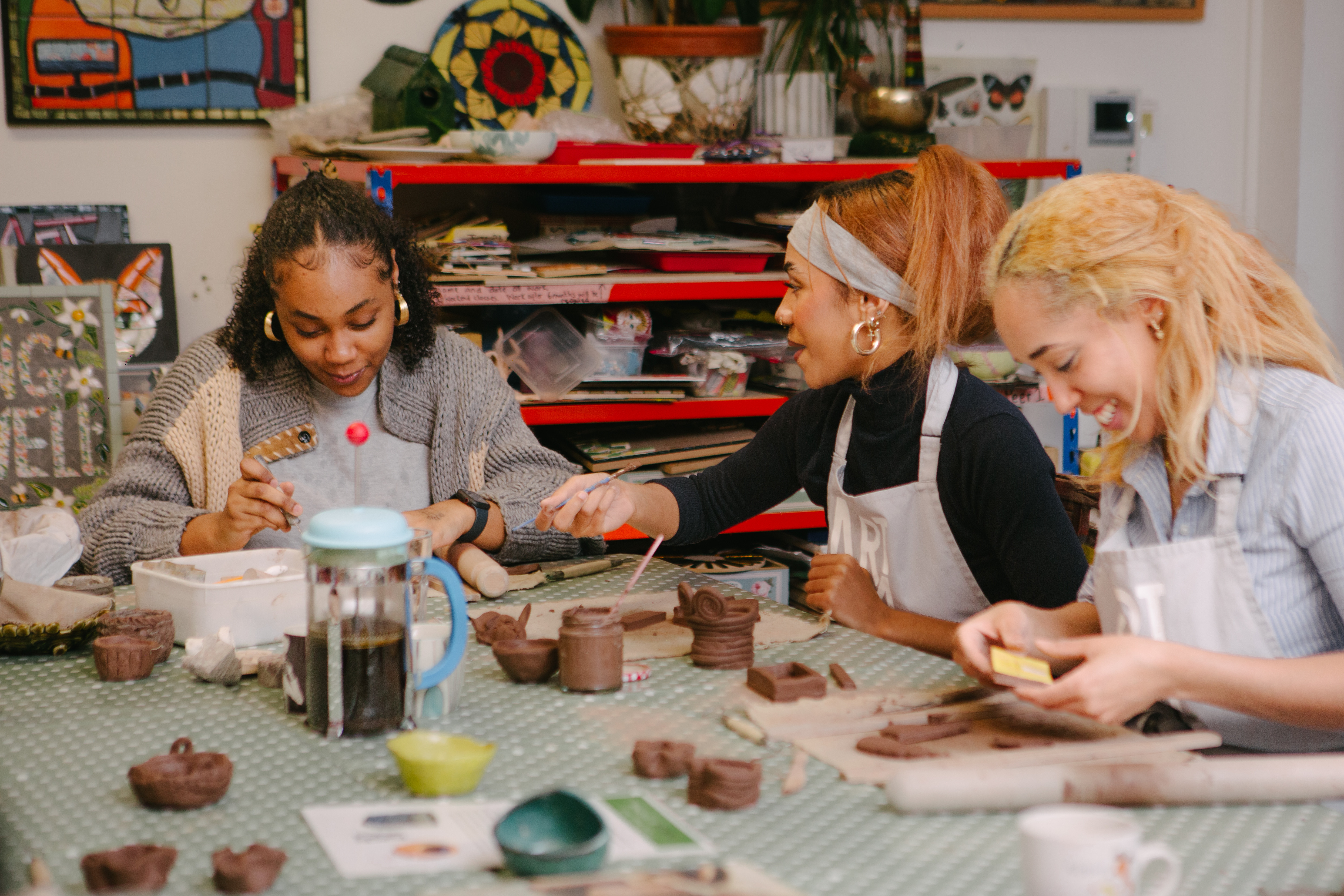 Three women sitting at a table are making clay pots using hand building techniques